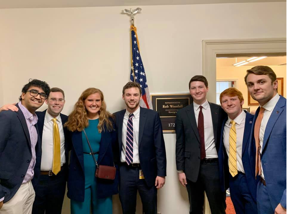 Several students stand in front of a Congressional office, wearing business attire.